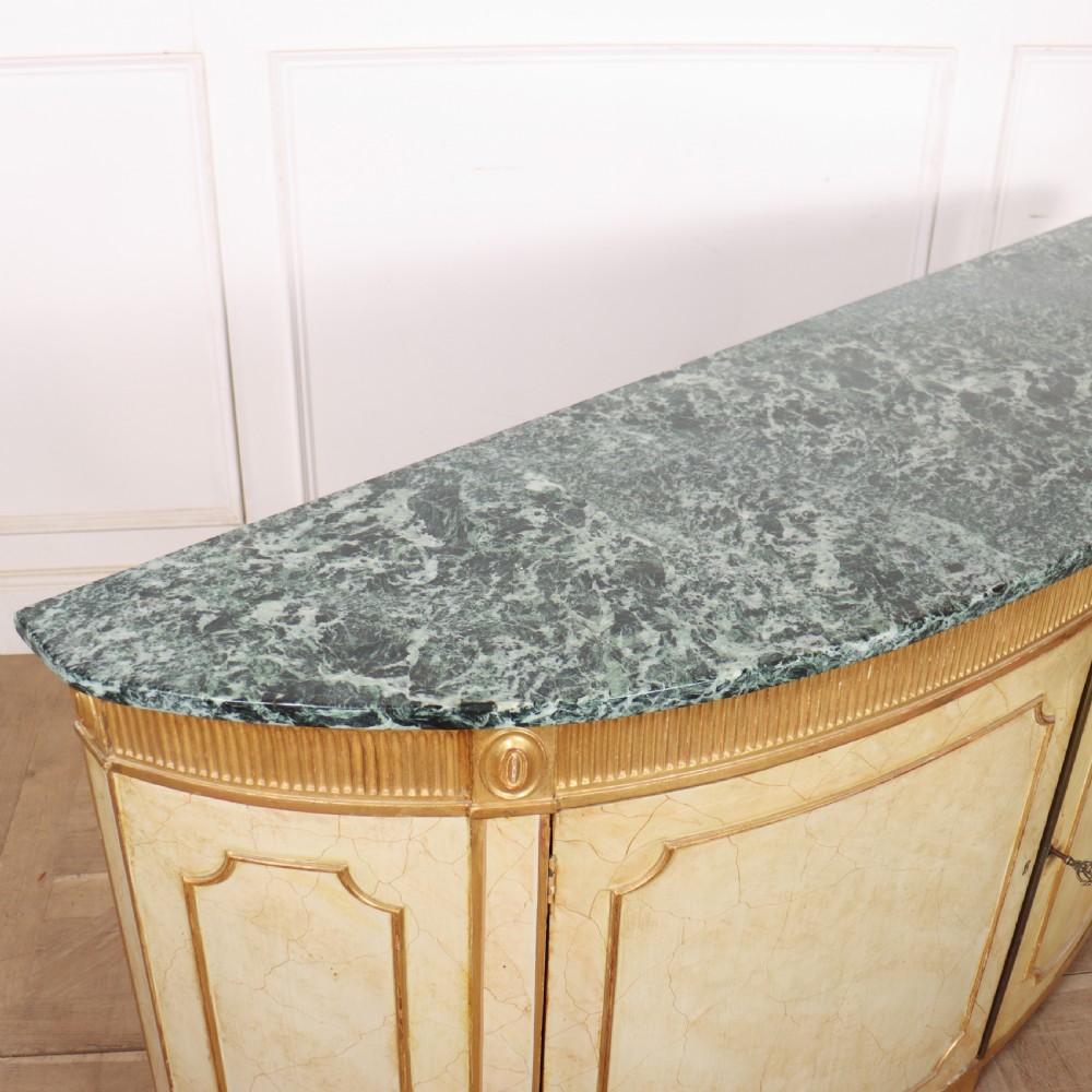A Neoclassical style cream painted demi-lune side cabinet featuring a dark green marble top, fluted gilded frieze, and panelled cupboard doors. View XI