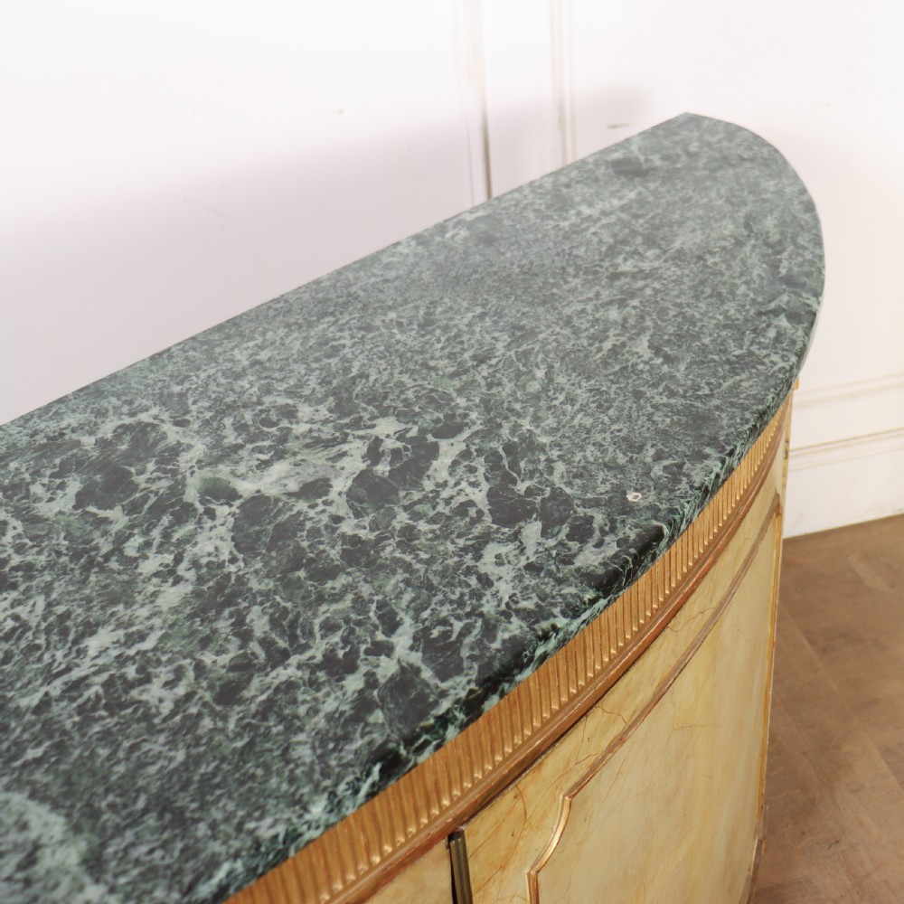 A Neoclassical style cream painted demi-lune side cabinet featuring a dark green marble top, fluted gilded frieze, and panelled cupboard doors. View XII