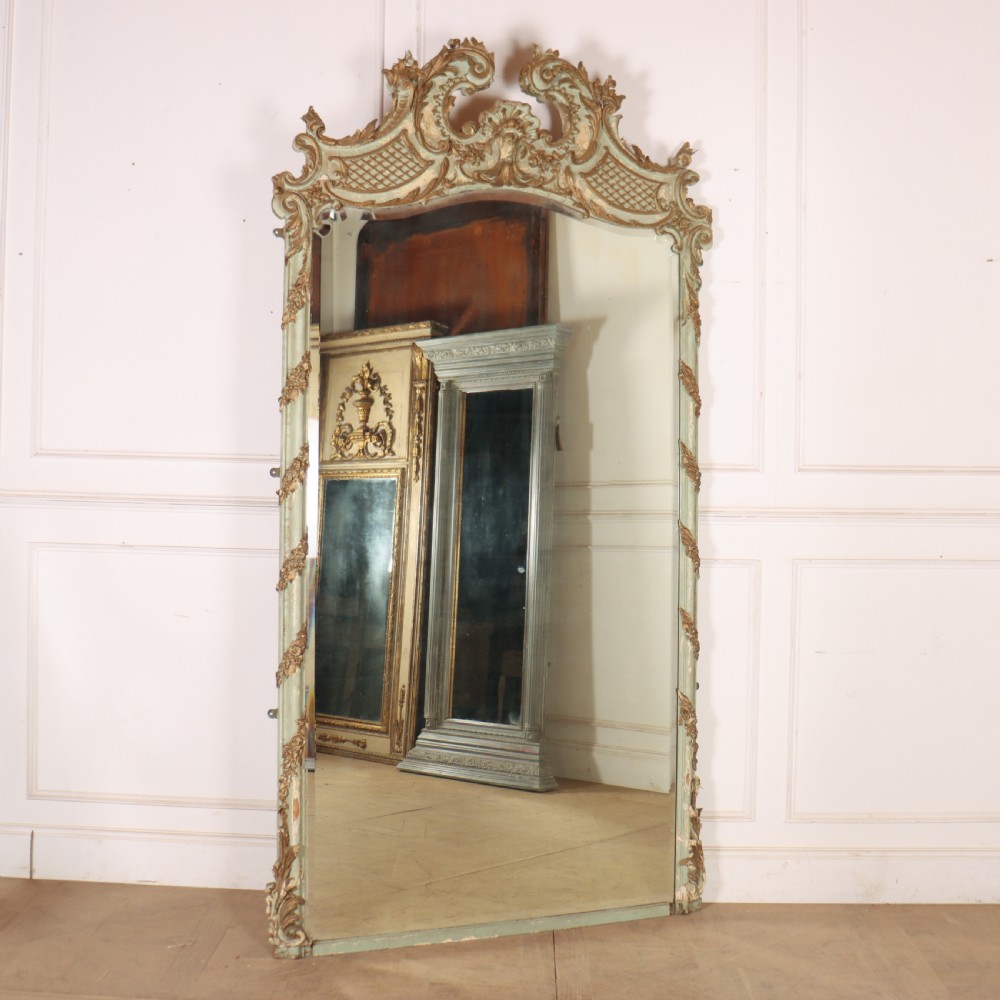 A tall French Rococo style mirror featuring an arched frame painted in pale grey-green with carved giltwood C-scrolls, lattice work, and foliate garlands.