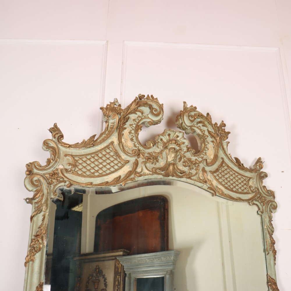 A tall French Rococo style mirror featuring an arched frame painted in pale grey-green with carved giltwood C-scrolls, lattice work, and foliate garlands. View IV