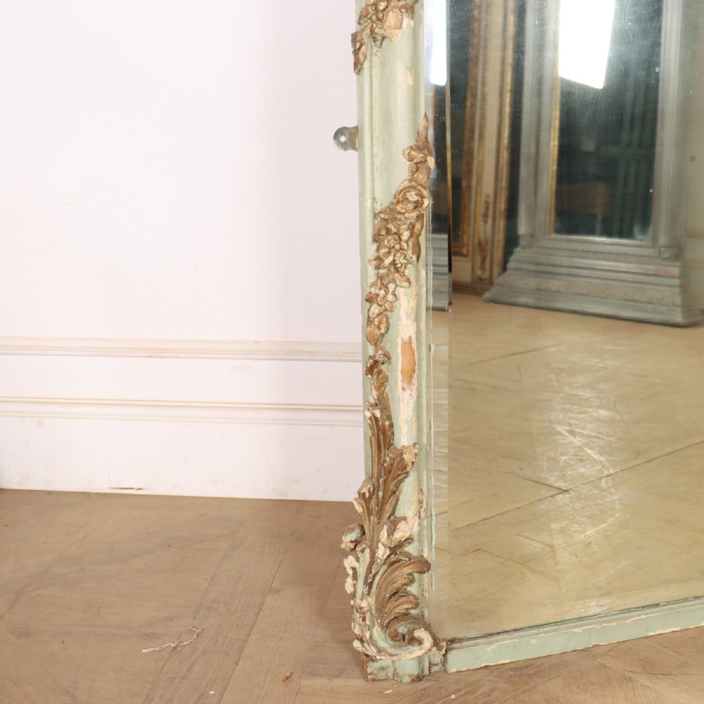 A tall French Rococo style mirror featuring an arched frame painted in pale grey-green with carved giltwood C-scrolls, lattice work, and foliate garlands. View V
