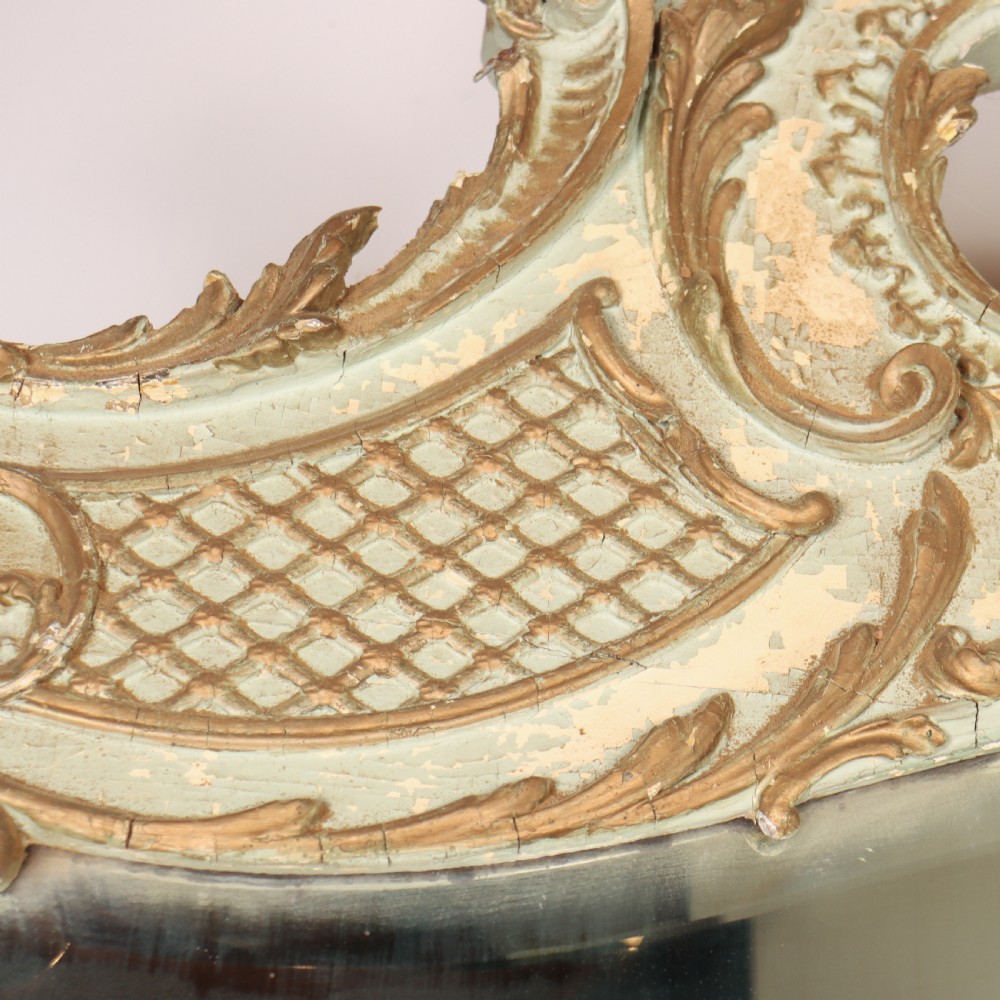 A tall French Rococo style mirror featuring an arched frame painted in pale grey-green with carved giltwood C-scrolls, lattice work, and foliate garlands. View IX