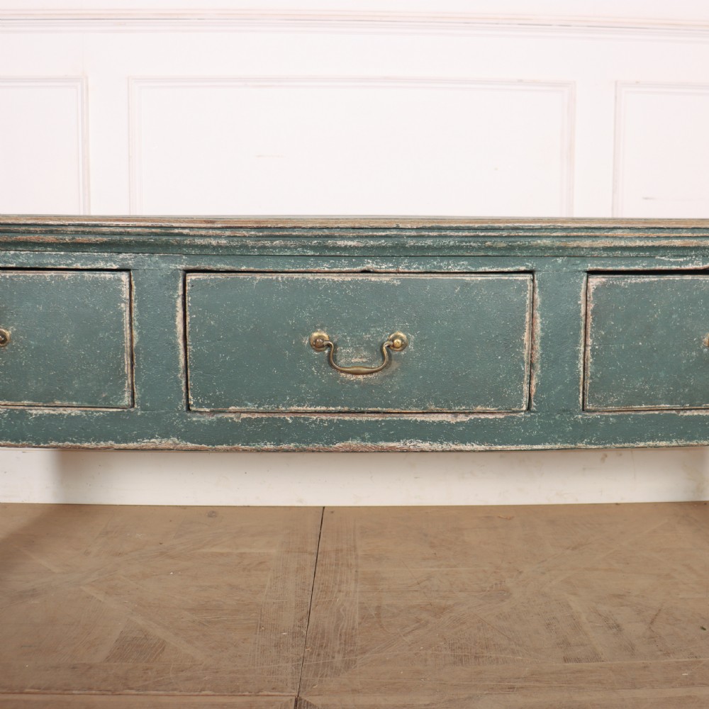 An English wooden dresser base painted in distressed muted green with three drawers and brass swan-neck handles. View II