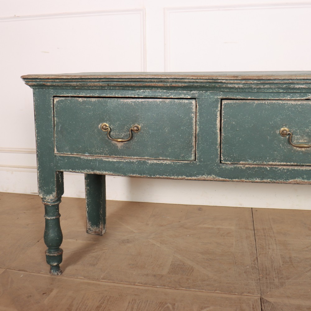 An English wooden dresser base painted in distressed muted green with three drawers and brass swan-neck handles. View III