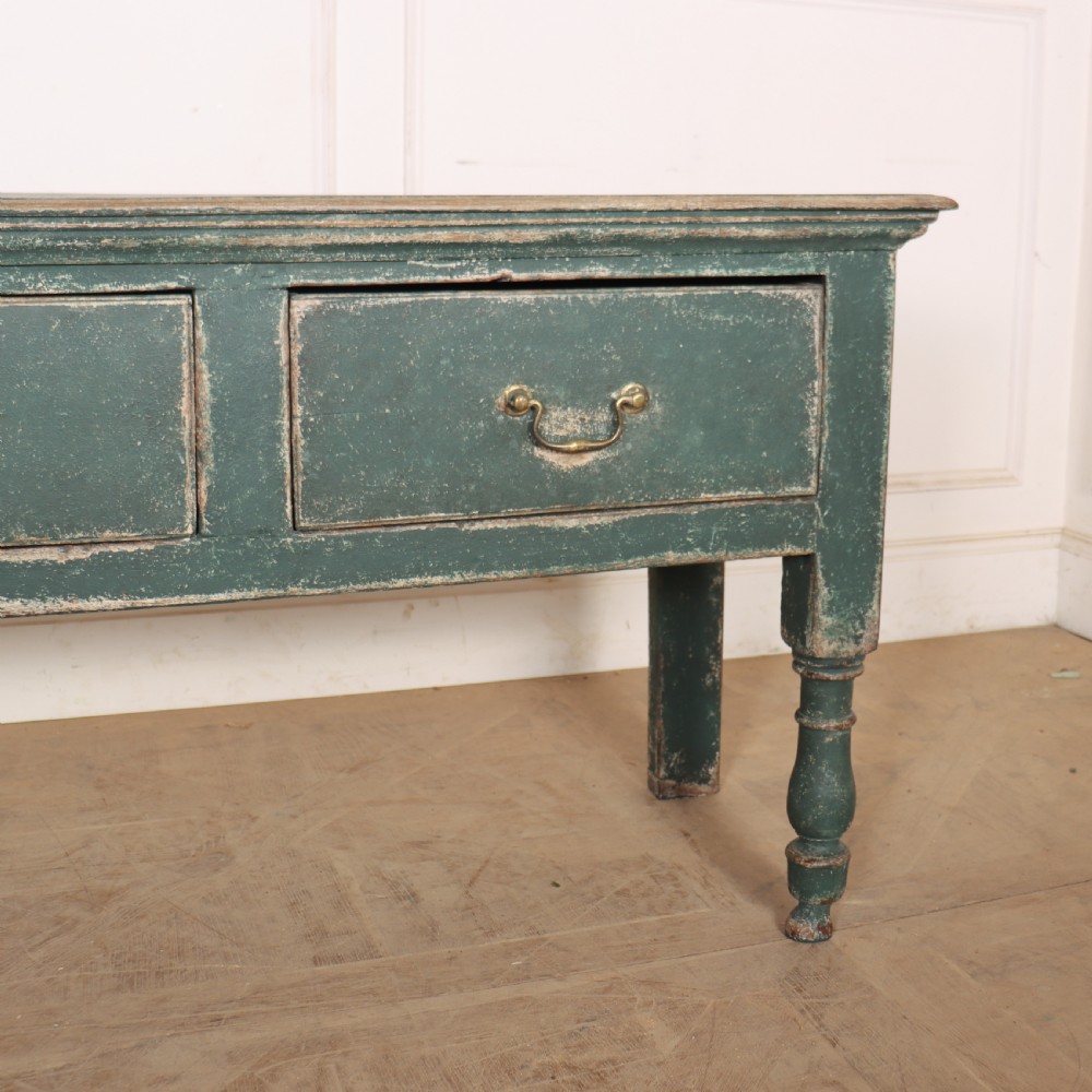 An English wooden dresser base painted in distressed muted green with three drawers and brass swan-neck handles. View IV