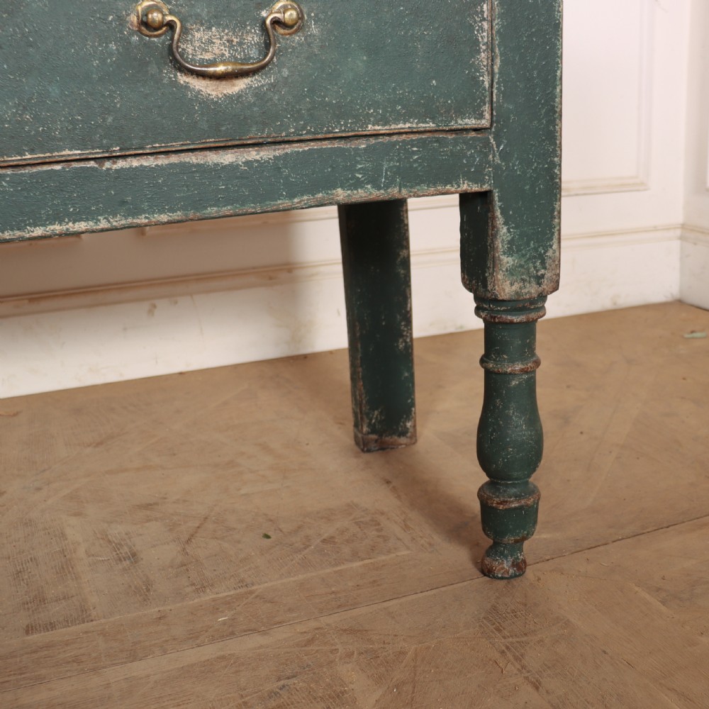 An English wooden dresser base painted in distressed muted green with three drawers and brass swan-neck handles. View V