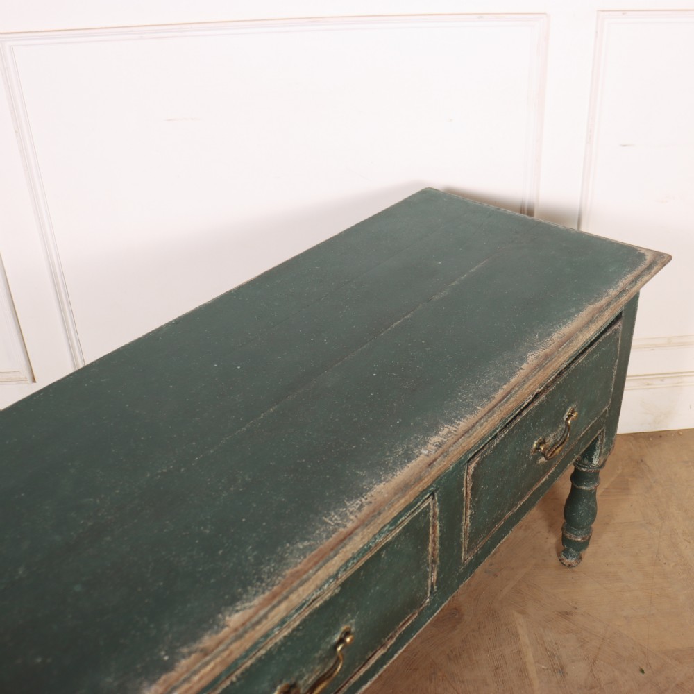 An English wooden dresser base painted in distressed muted green with three drawers and brass swan-neck handles. View XIII