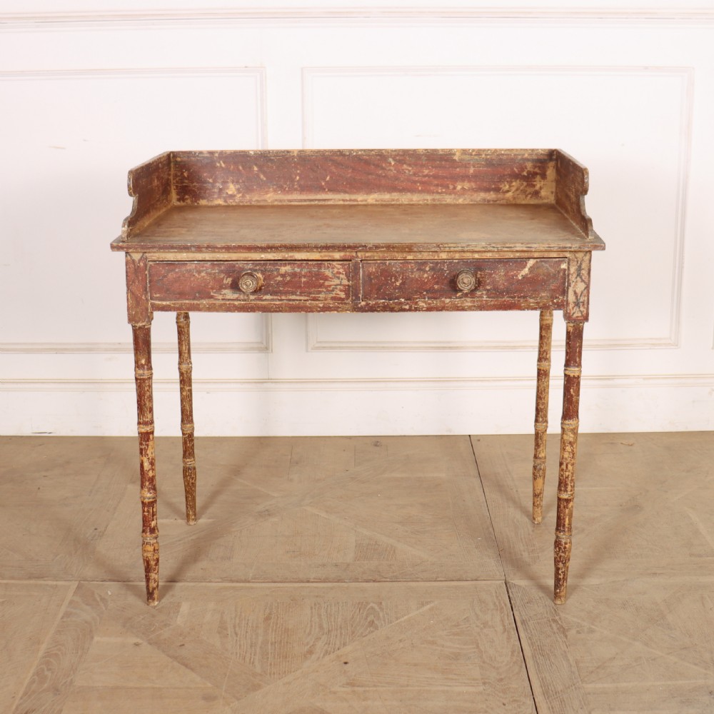 An antique English Regency painted side table featuring a gallery back, two front drawers, and turned faux bamboo legs with a distressed red and cream finish.