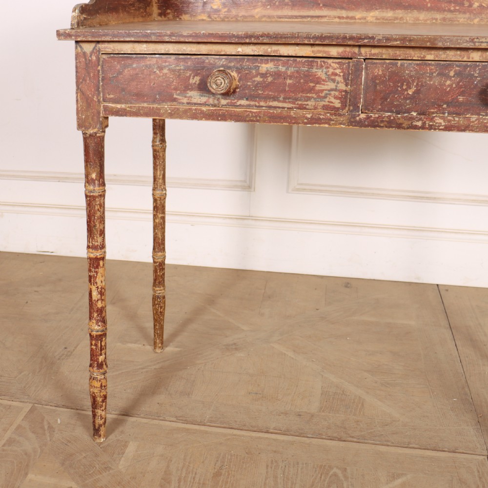 An antique English Regency painted side table featuring a gallery back, two front drawers, and turned faux bamboo legs with a distressed red and cream finish. View II