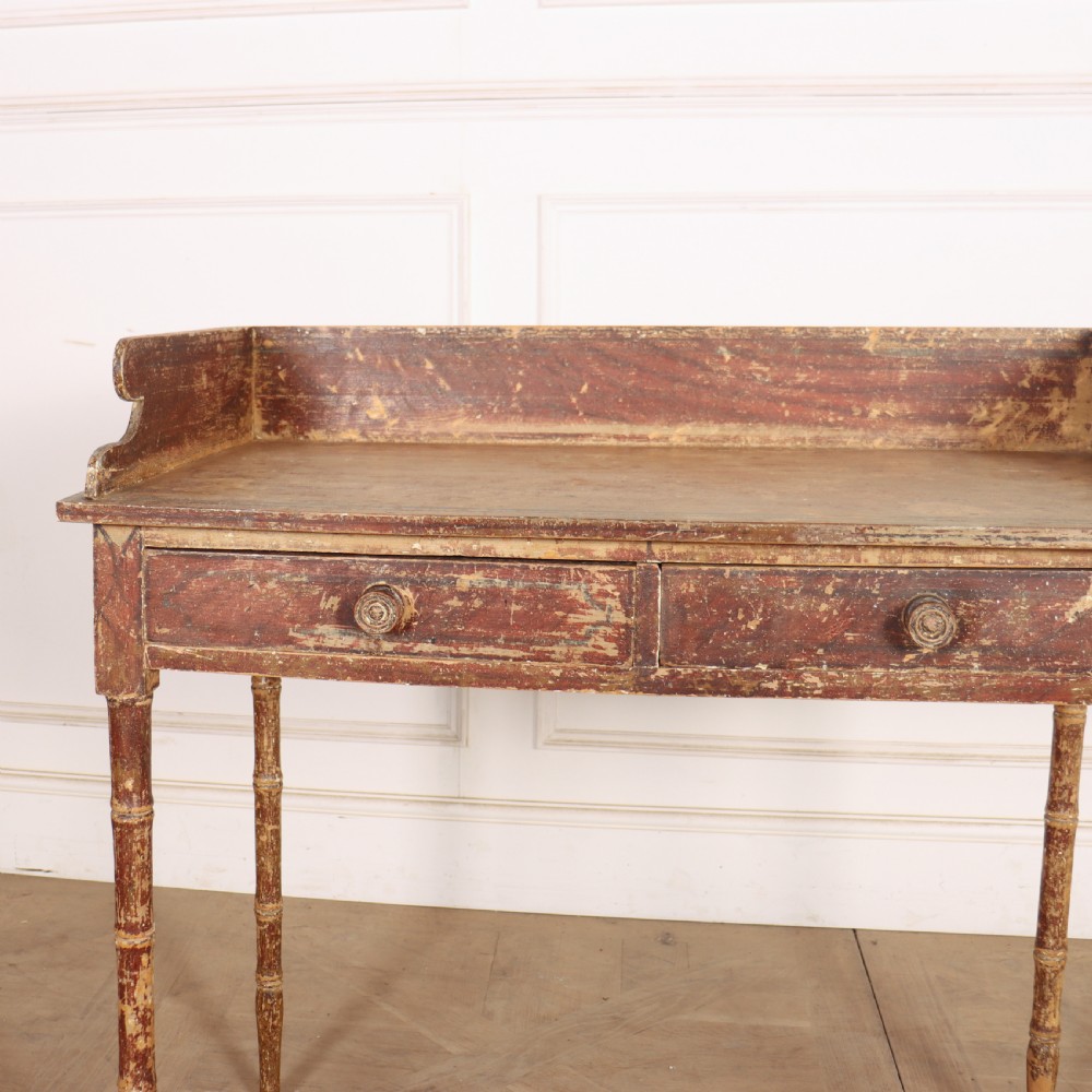 An antique English Regency painted side table featuring a gallery back, two front drawers, and turned faux bamboo legs with a distressed red and cream finish. View III