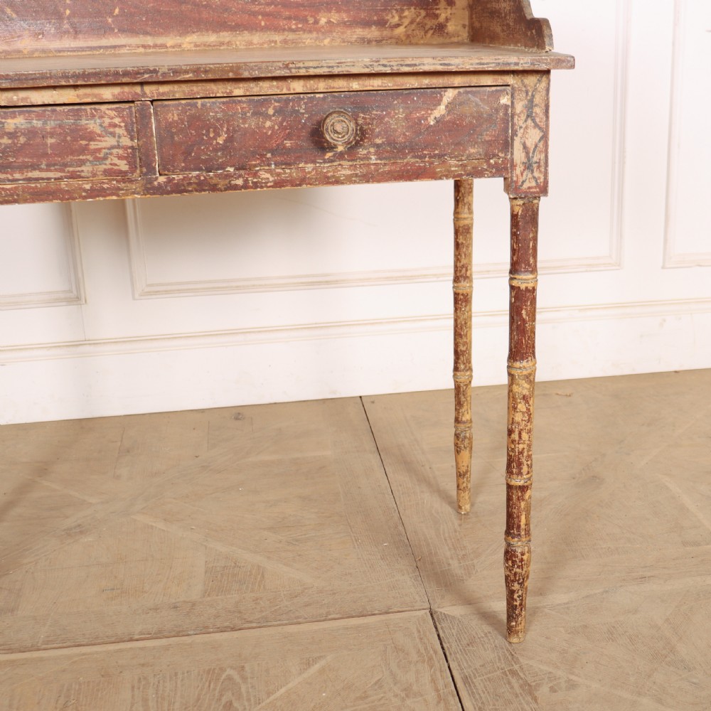 An antique English Regency painted side table featuring a gallery back, two front drawers, and turned faux bamboo legs with a distressed red and cream finish. View IV