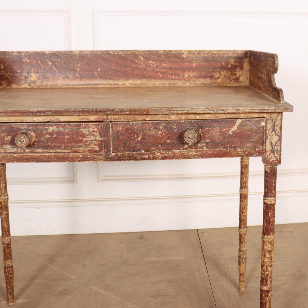 An antique English Regency painted side table featuring a gallery back, two front drawers, and turned faux bamboo legs with a distressed red and cream finish. View V