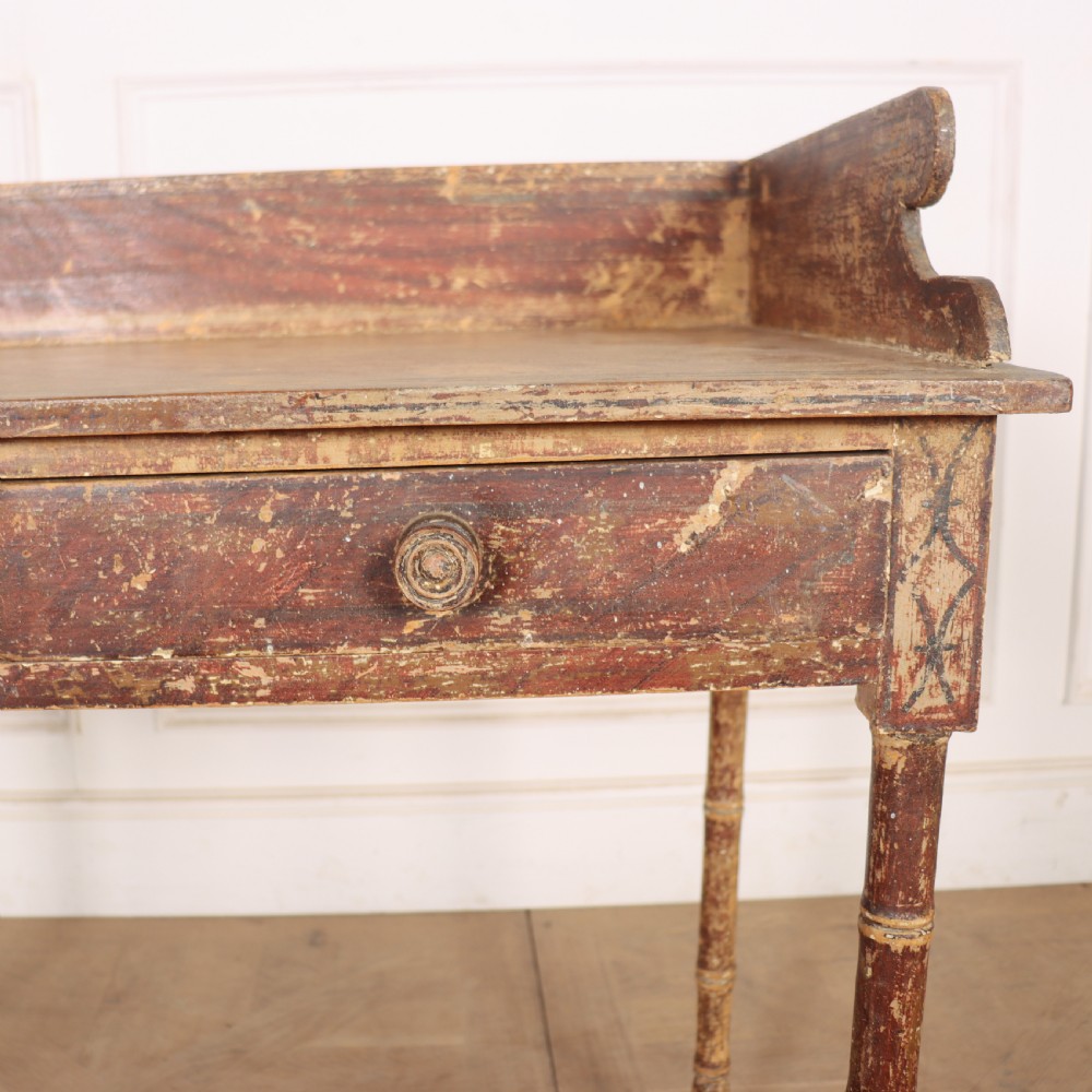 An antique English Regency painted side table featuring a gallery back, two front drawers, and turned faux bamboo legs with a distressed red and cream finish. View VI