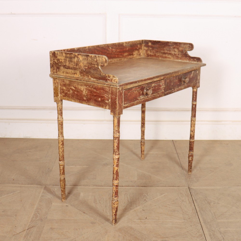 An antique English Regency painted side table featuring a gallery back, two front drawers, and turned faux bamboo legs with a distressed red and cream finish. View VII