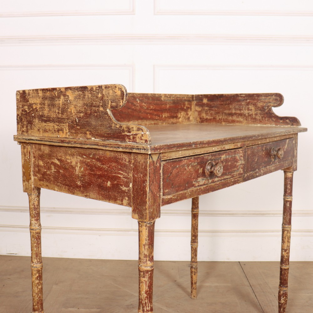 An antique English Regency painted side table featuring a gallery back, two front drawers, and turned faux bamboo legs with a distressed red and cream finish. View VIII