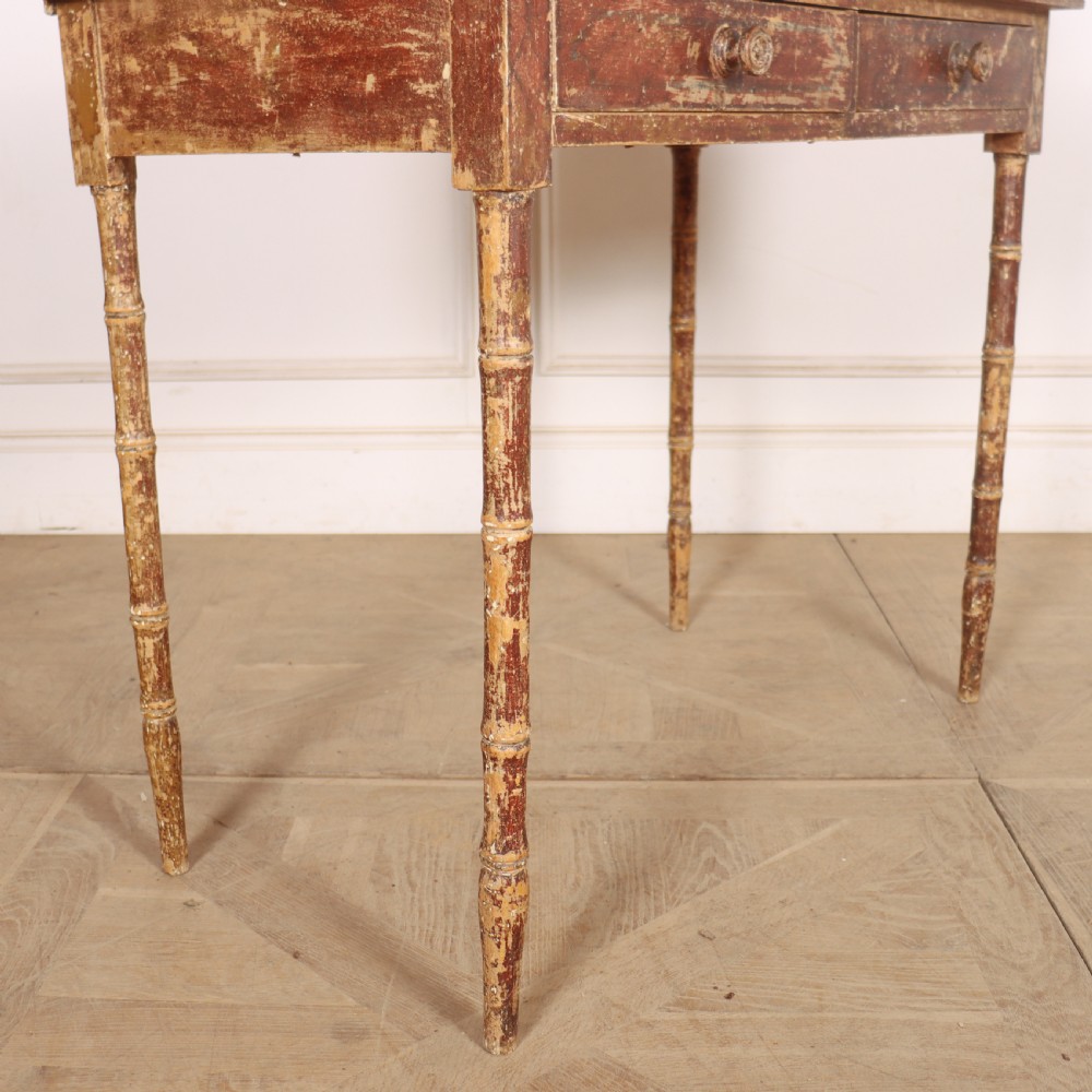An antique English Regency painted side table featuring a gallery back, two front drawers, and turned faux bamboo legs with a distressed red and cream finish. View IX