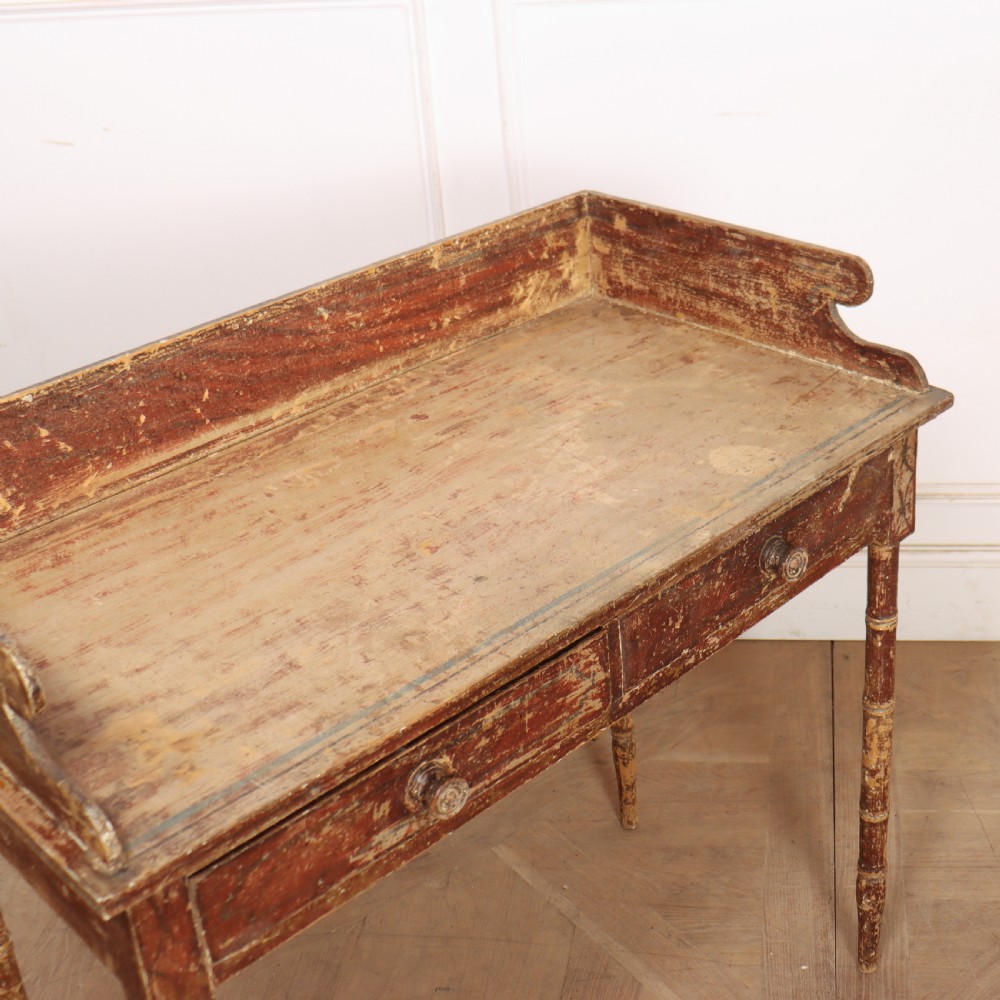 An antique English Regency painted side table featuring a gallery back, two front drawers, and turned faux bamboo legs with a distressed red and cream finish. View X