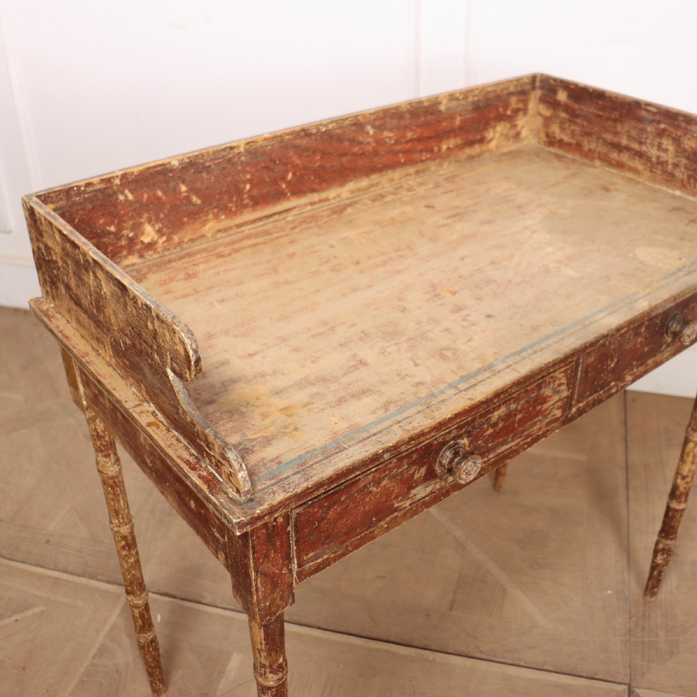 An antique English Regency painted side table featuring a gallery back, two front drawers, and turned faux bamboo legs with a distressed red and cream finish. View XI