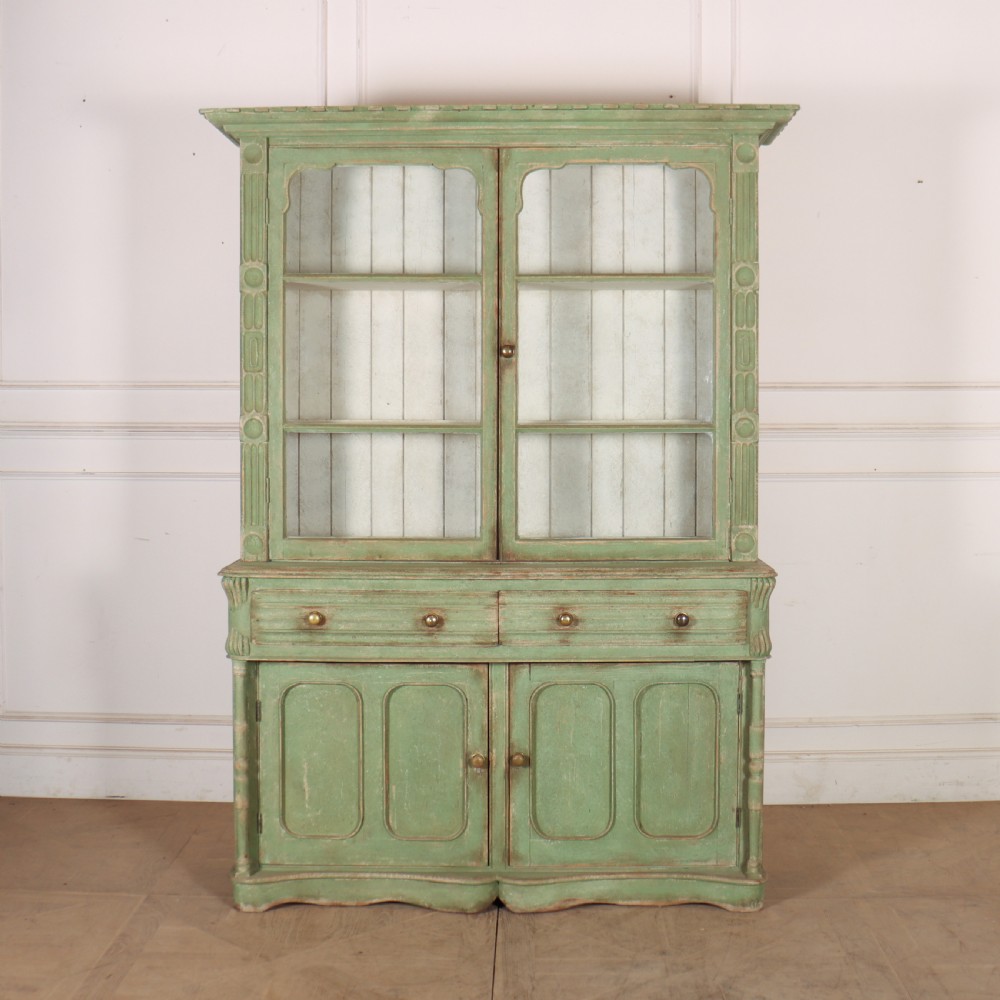 An antique West Country kitchen dresser in distressed sage green paint, featuring upper glazed doors and lower panelled cupboards.