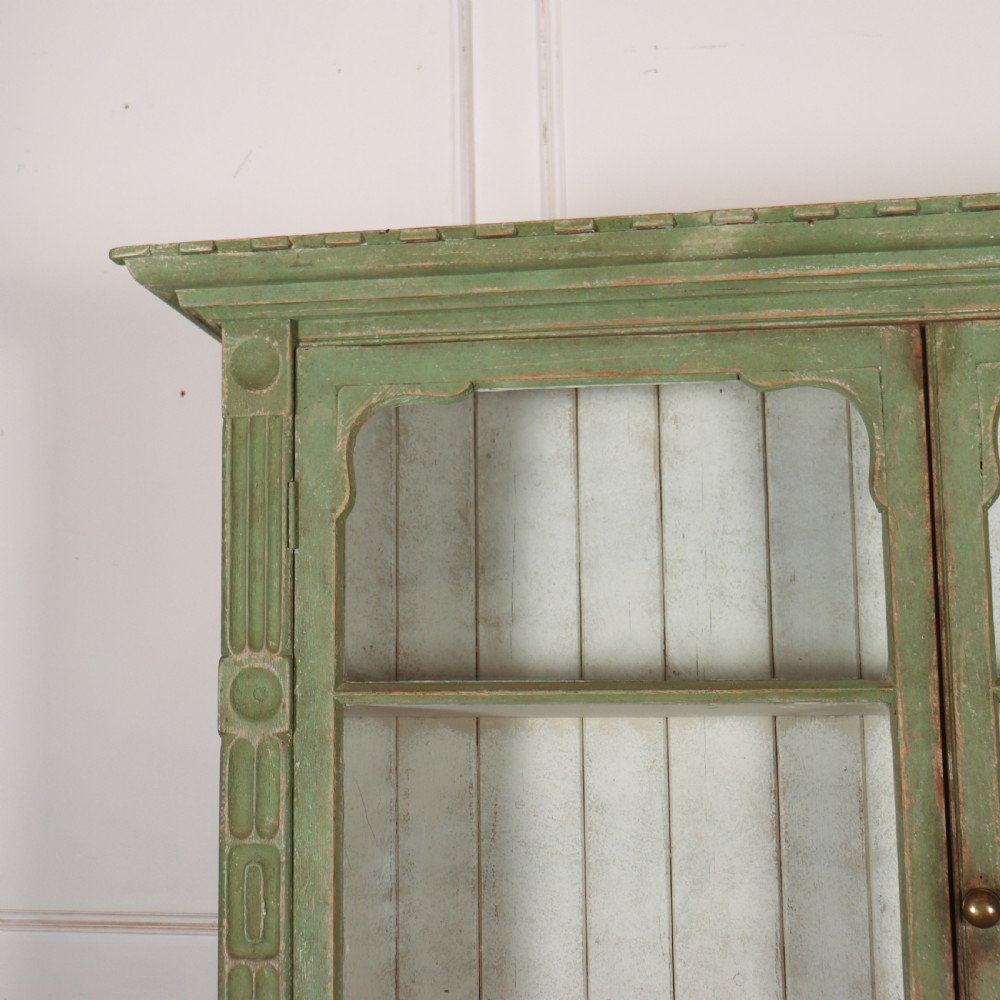 An antique West Country kitchen dresser in distressed sage green paint, featuring upper glazed doors and lower panelled cupboards. View III