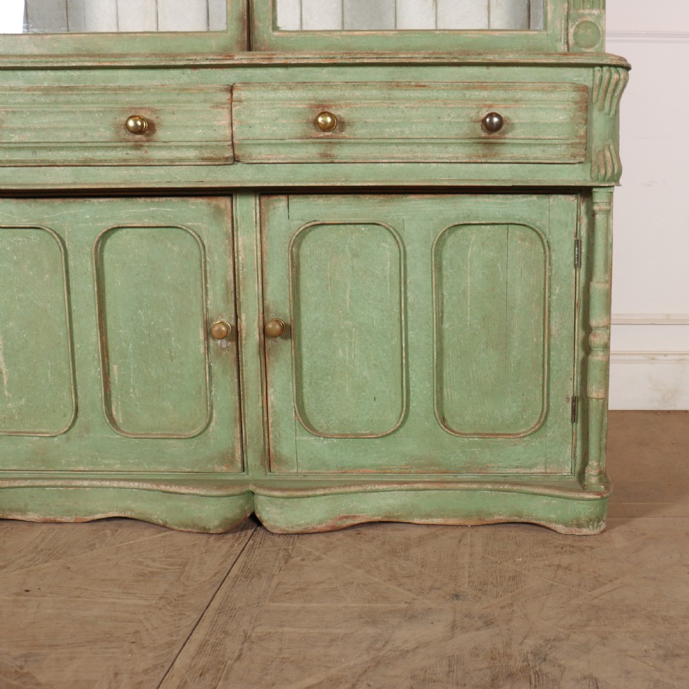 An antique West Country kitchen dresser in distressed sage green paint, featuring upper glazed doors and lower panelled cupboards. View V