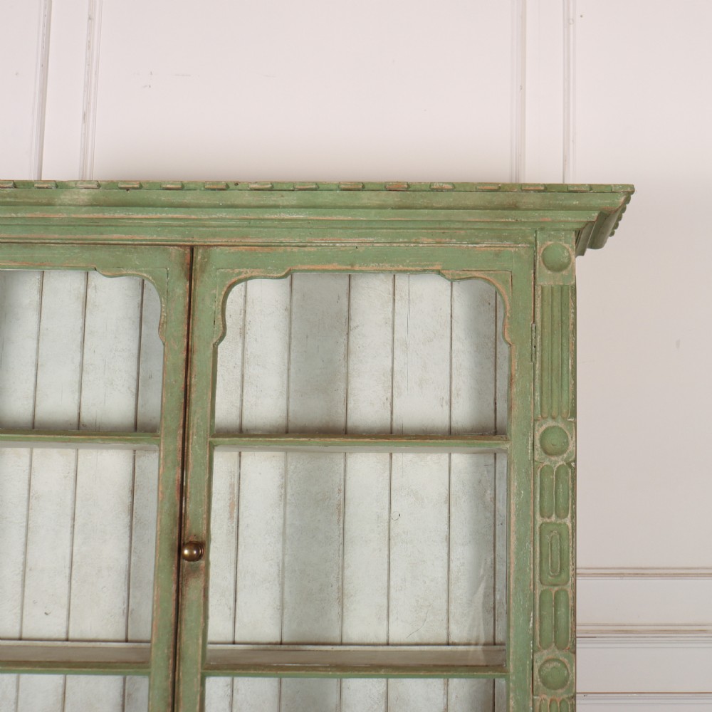 An antique West Country kitchen dresser in distressed sage green paint, featuring upper glazed doors and lower panelled cupboards. View VI
