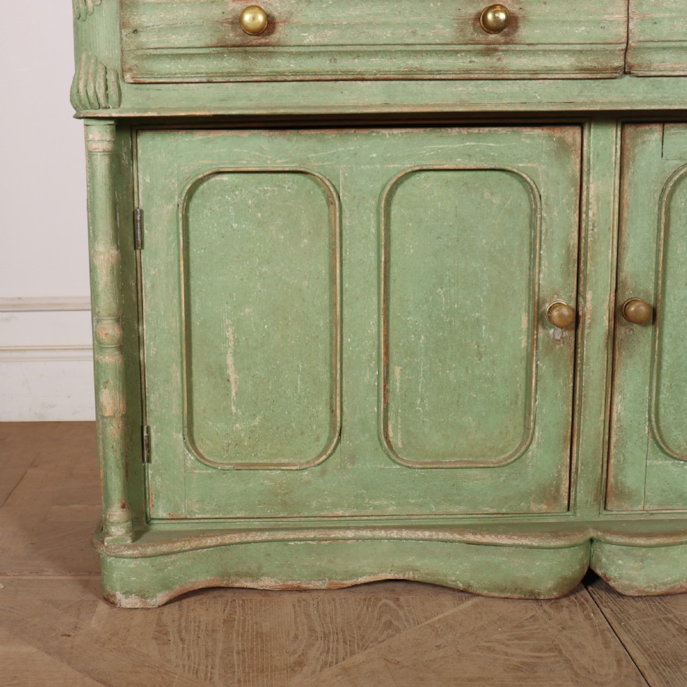An antique West Country kitchen dresser in distressed sage green paint, featuring upper glazed doors and lower panelled cupboards. View VIII