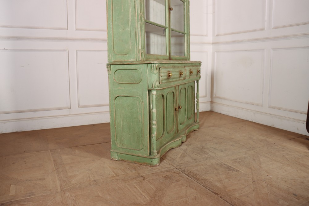 An antique West Country kitchen dresser in distressed sage green paint, featuring upper glazed doors and lower panelled cupboards. View X