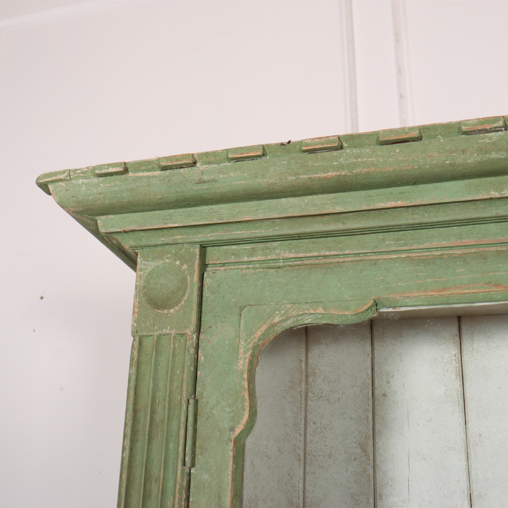 An antique West Country kitchen dresser in distressed sage green paint, featuring upper glazed doors and lower panelled cupboards. View XII