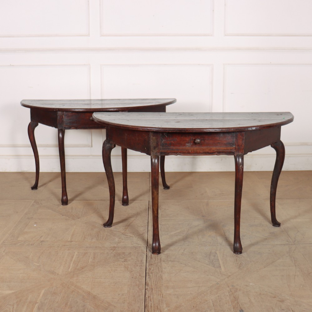 A pair of dark wood demi-lune console tables featuring semi-circular tops, single frieze drawers, and slender cabriole legs.