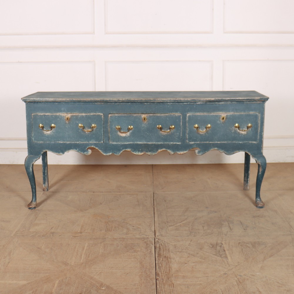 An antique blue-painted dresser base featuring three drawers with brass drop handles, a scalloped apron, and cabriole legs.