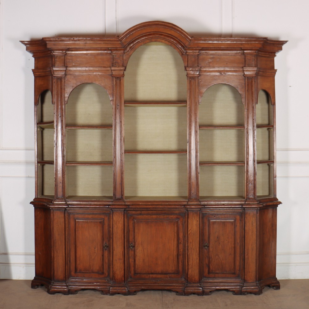 A large 1920s Italian walnut breakfront bookcase with open arched upper shelving and panelled lower cupboard doors.