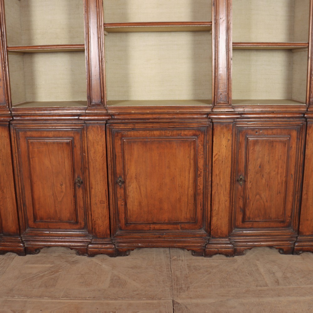 A large 1920s Italian walnut breakfront bookcase with open arched upper shelving and panelled lower cupboard doors. View VI