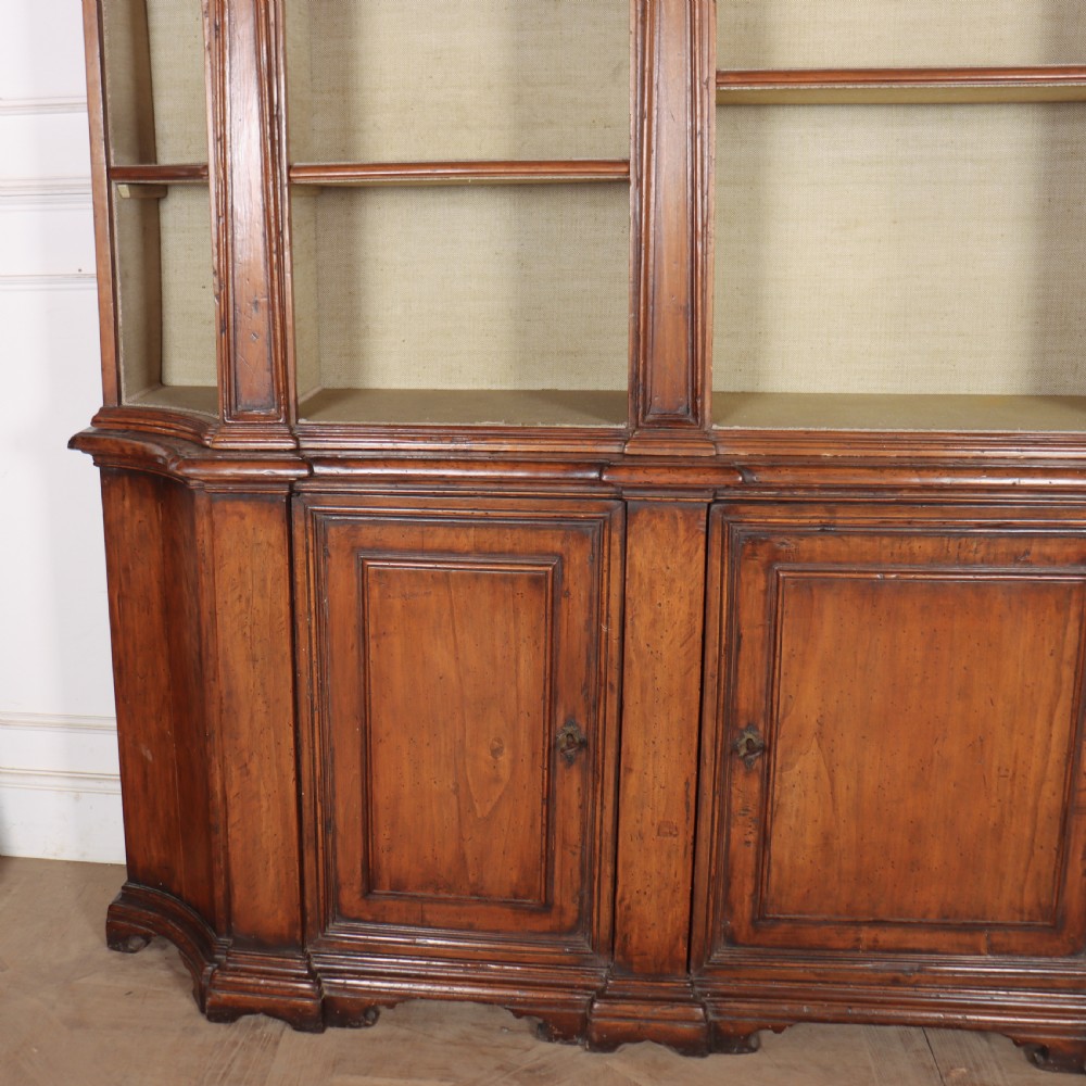 A large 1920s Italian walnut breakfront bookcase with open arched upper shelving and panelled lower cupboard doors. View VII