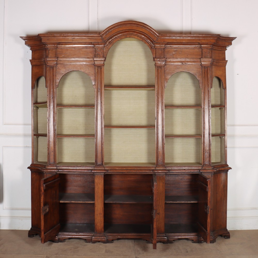 A large 1920s Italian walnut breakfront bookcase with open arched upper shelving and panelled lower cupboard doors. View IX