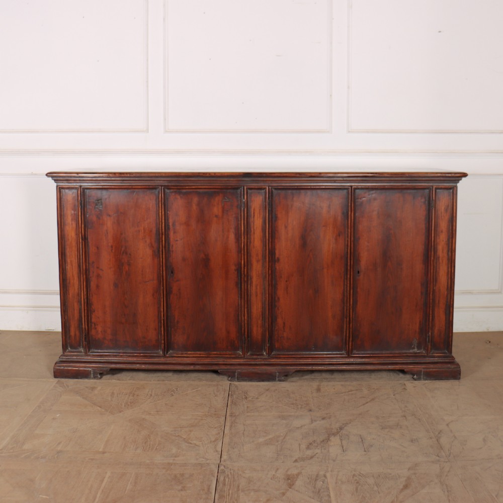A large antique Italian dark walnut sideboard featuring four moulded rectangular panel doors and a solid plinth base.