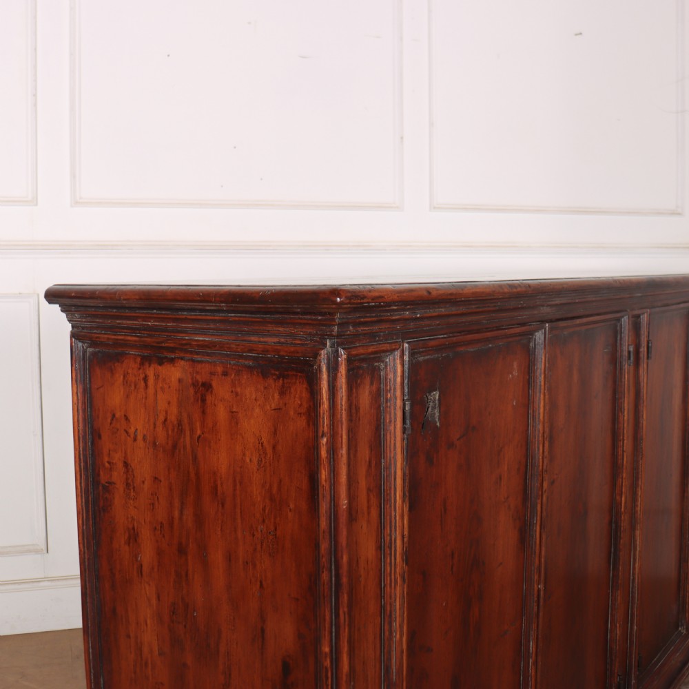 A large antique Italian dark walnut sideboard featuring four moulded rectangular panel doors and a solid plinth base. View X