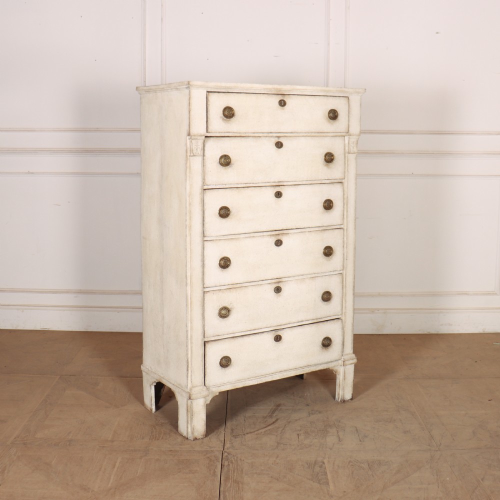 An off-white painted tallboy chest of drawers featuring six stacked drawers with round brass handles and keyhole escutcheons. View X