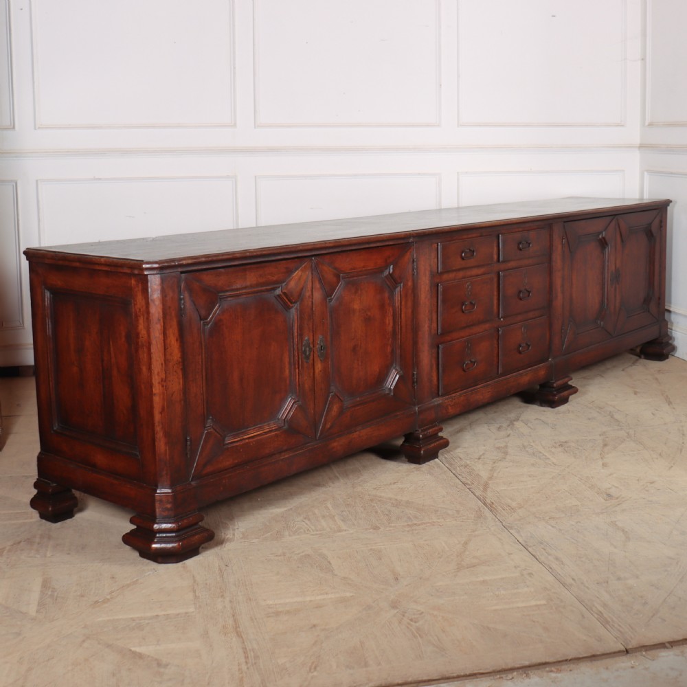 A long, monumental dark walnut Italian credenza featuring geometric moulded panel doors, a central column of drawers, and carved plinth feet.