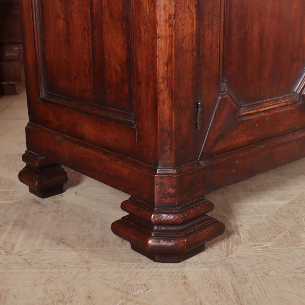 A long, monumental dark walnut Italian credenza featuring geometric moulded panel doors, a central column of drawers, and carved plinth feet. View II