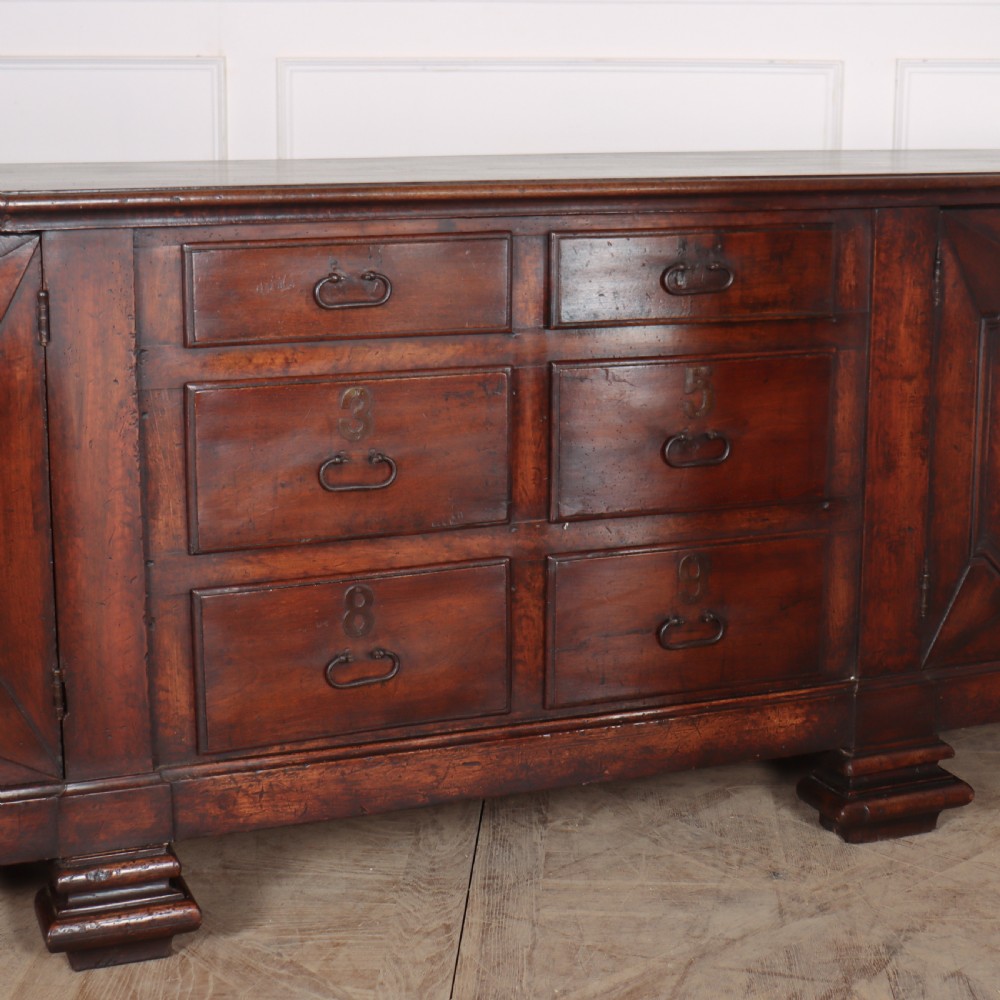 A long, monumental dark walnut Italian credenza featuring geometric moulded panel doors, a central column of drawers, and carved plinth feet. View V
