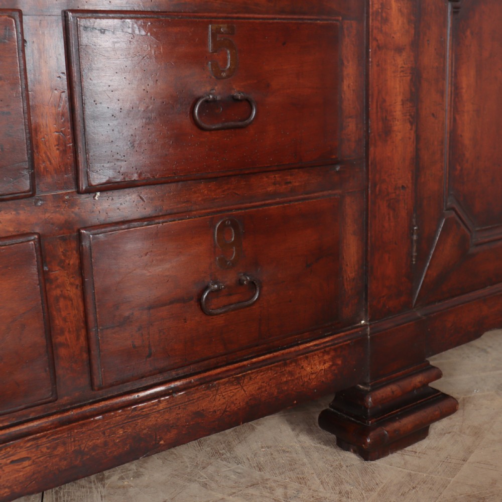 A long, monumental dark walnut Italian credenza featuring geometric moulded panel doors, a central column of drawers, and carved plinth feet. View VII