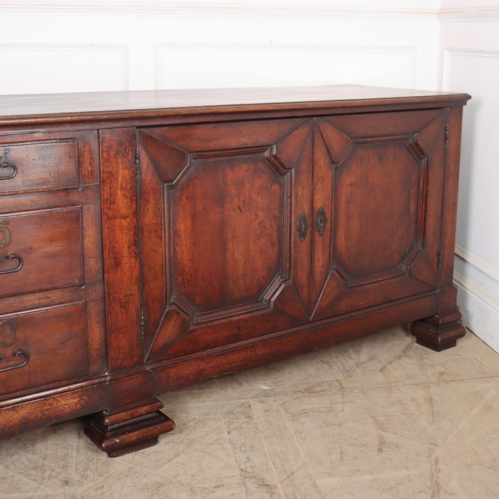 A long, monumental dark walnut Italian credenza featuring geometric moulded panel doors, a central column of drawers, and carved plinth feet. View VIII