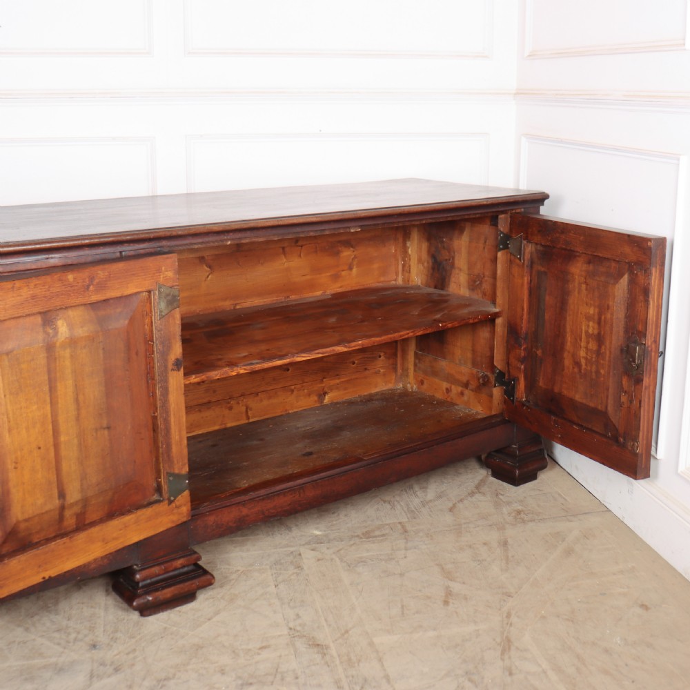 A long, monumental dark walnut Italian credenza featuring geometric moulded panel doors, a central column of drawers, and carved plinth feet. View IX
