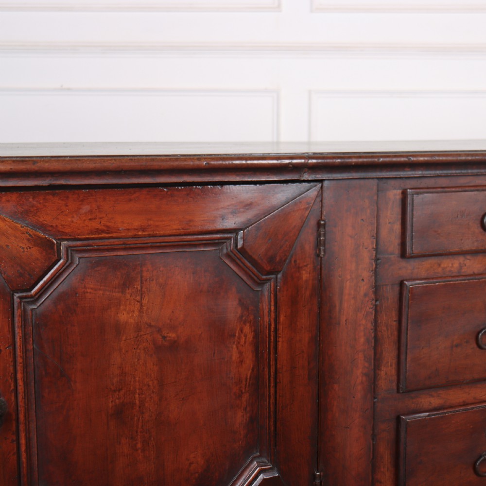A long, monumental dark walnut Italian credenza featuring geometric moulded panel doors, a central column of drawers, and carved plinth feet. View XI