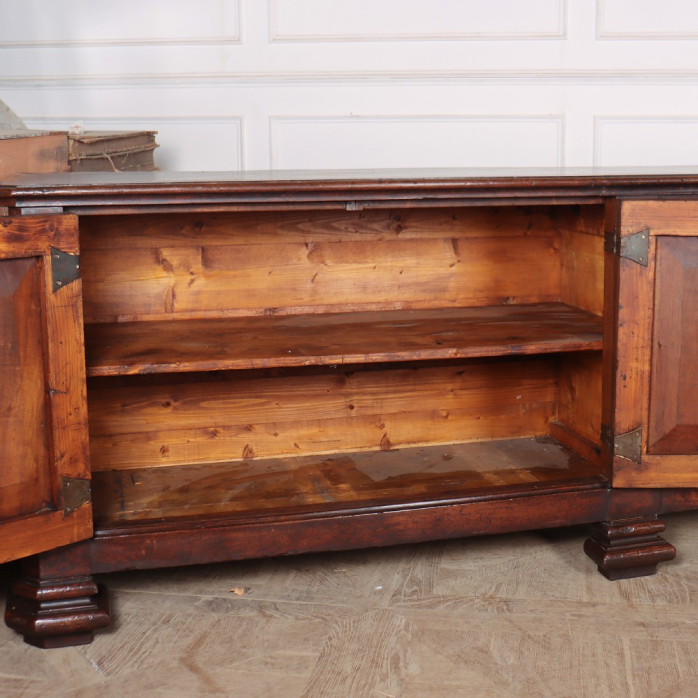 A long, monumental dark walnut Italian credenza featuring geometric moulded panel doors, a central column of drawers, and carved plinth feet. View XII