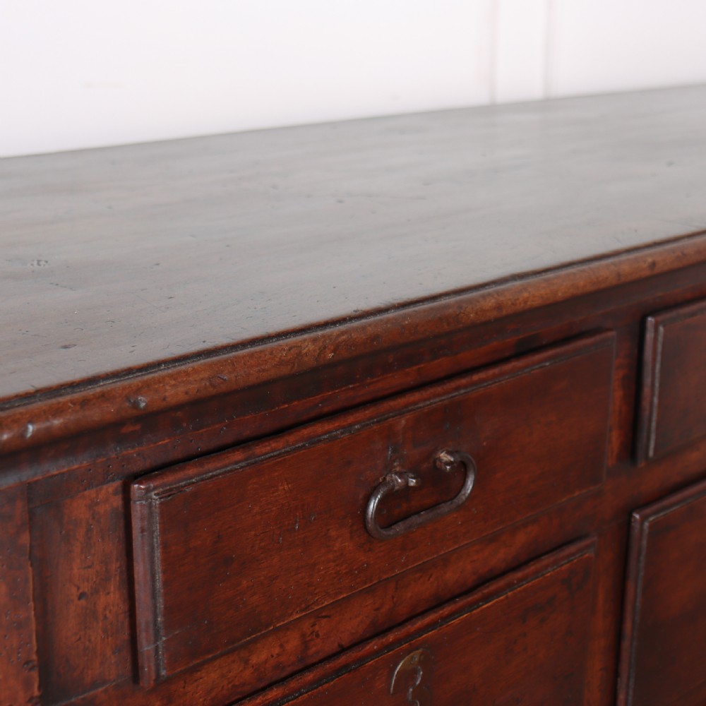 A long, monumental dark walnut Italian credenza featuring geometric moulded panel doors, a central column of drawers, and carved plinth feet. View XVI