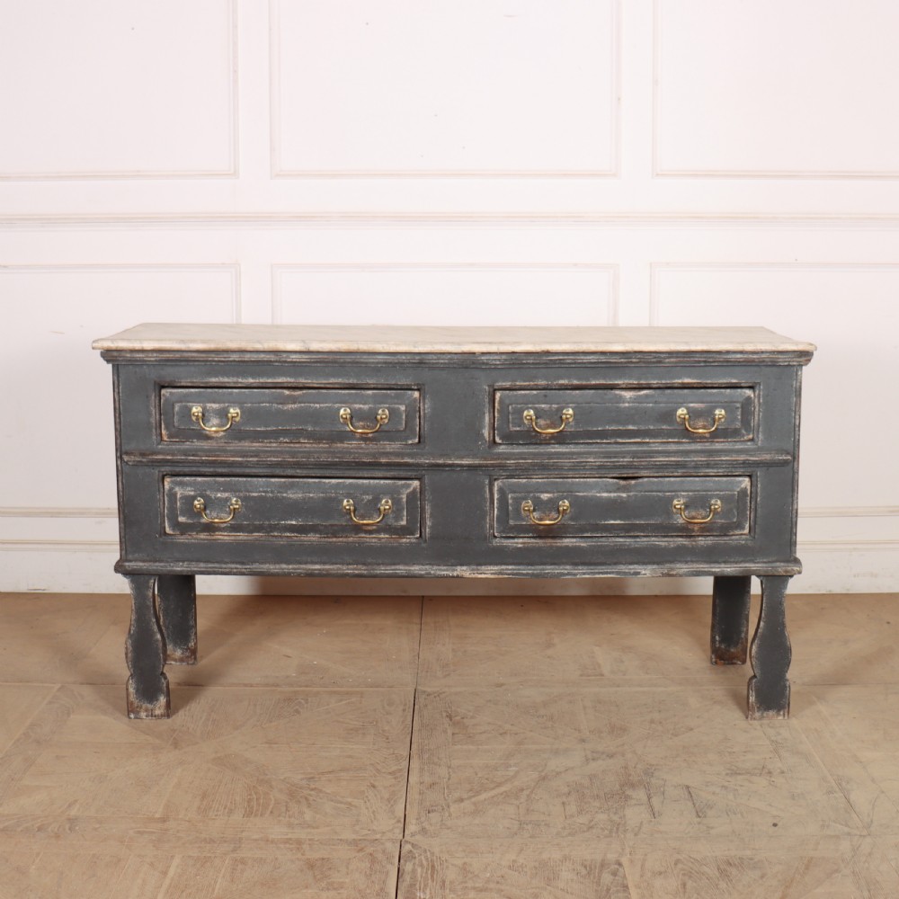 An English painted dresser base featuring a dark charcoal finish, four wide drawers with brass drop handles, shaped corner legs, and a light marble top.