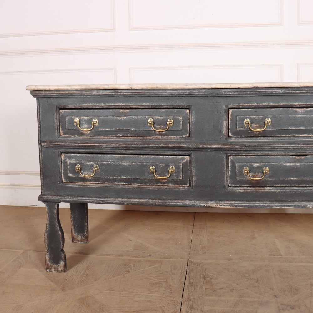 An English painted dresser base featuring a dark charcoal finish, four wide drawers with brass drop handles, shaped corner legs, and a light marble top. View II