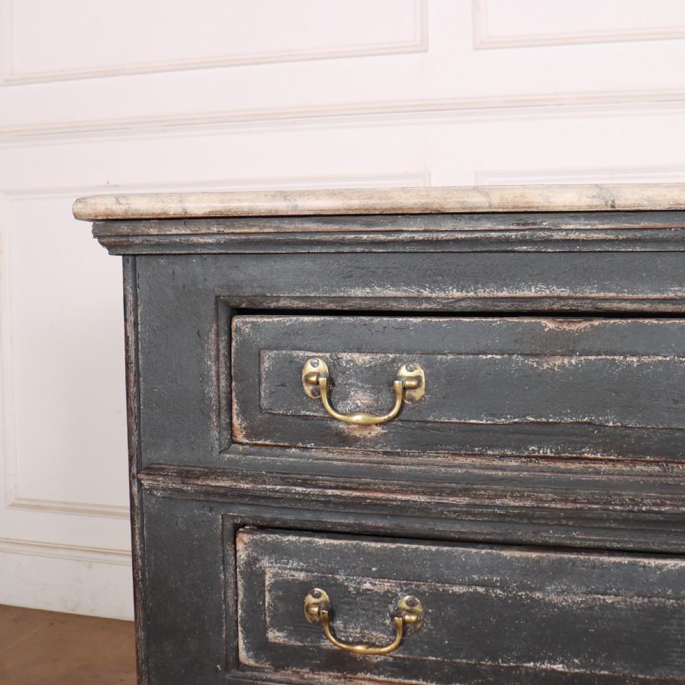 An English painted dresser base featuring a dark charcoal finish, four wide drawers with brass drop handles, shaped corner legs, and a light marble top. View IV